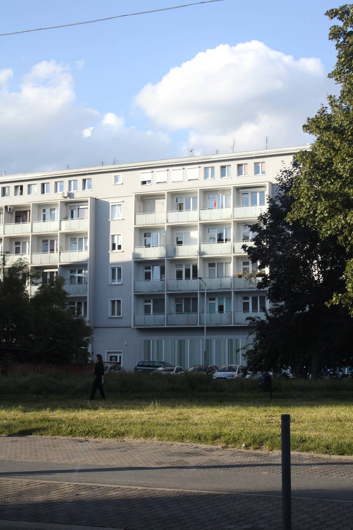 A woman walks in front of a white apartment building
