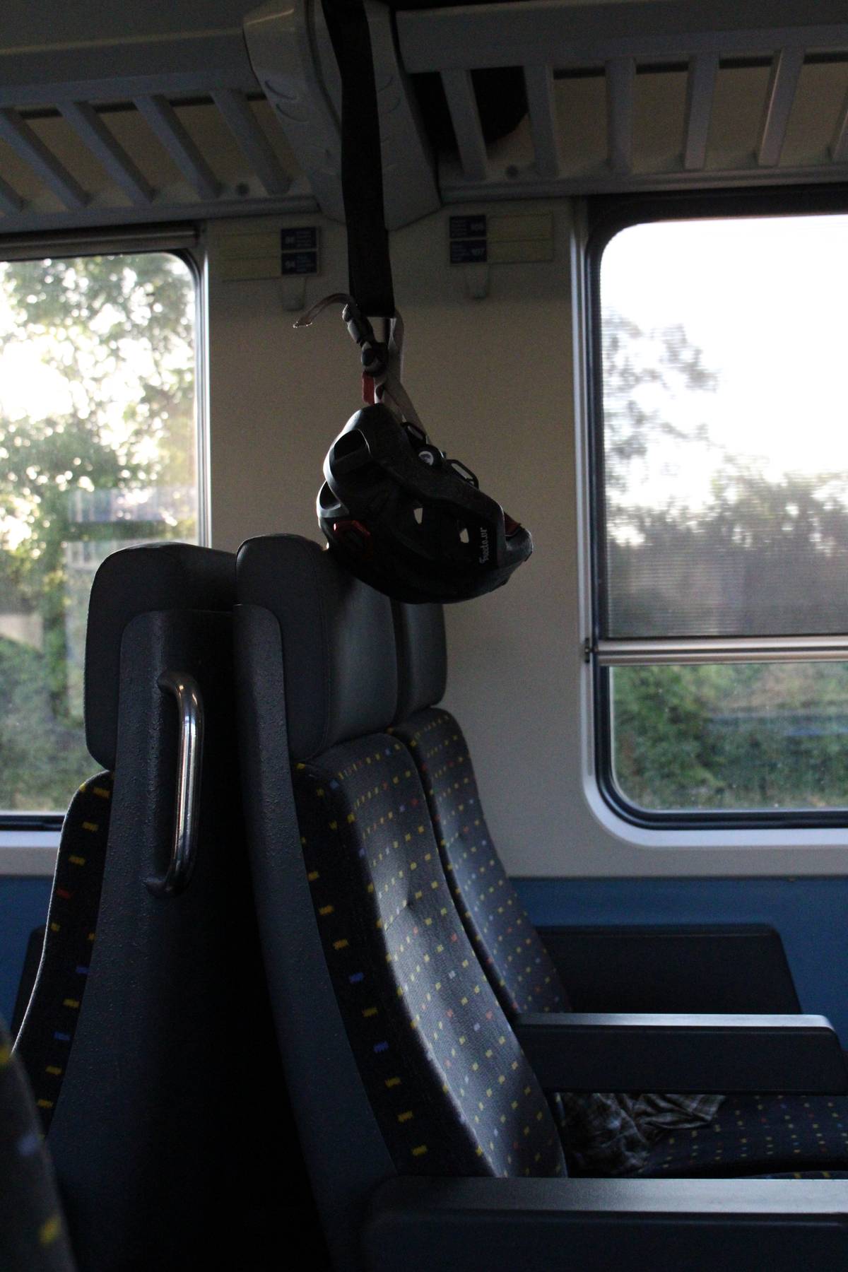 A helmet hangs from a train luggage rack
