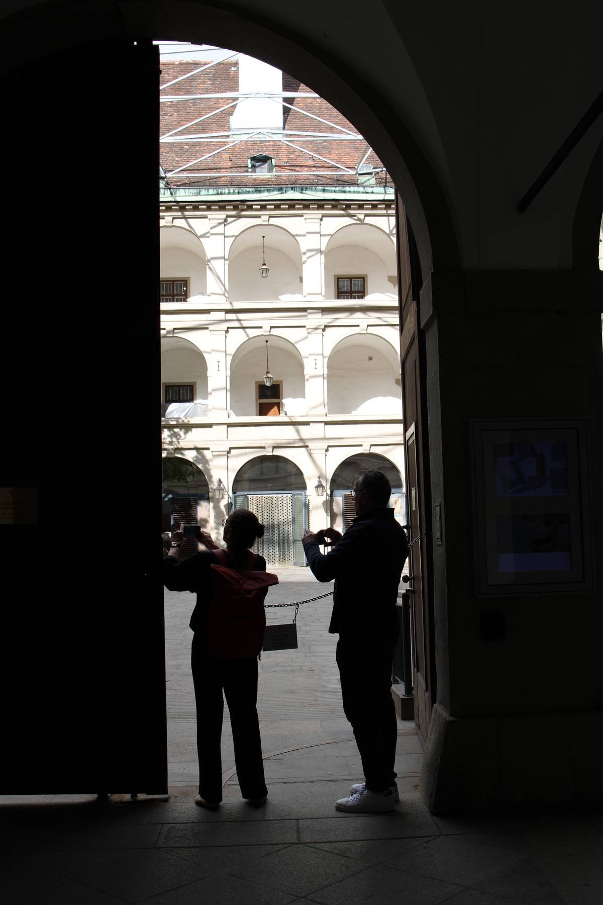 A couple photograph something with their phones. There is a bright building through the doorway, so the door arch and the couple are silhouetted.