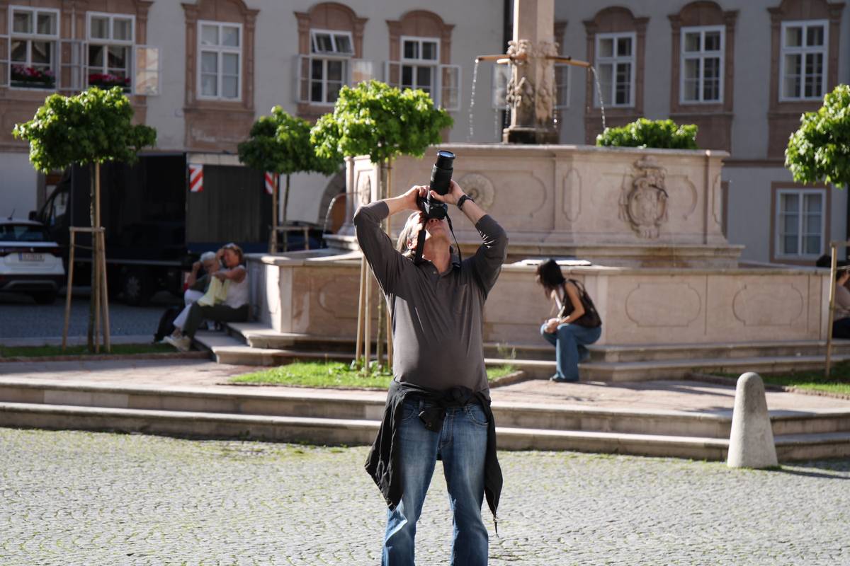A man takes a photograph of a church spire, and it's so high up that he's almost looking straight up.