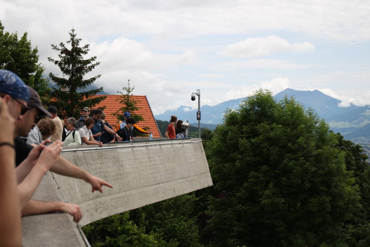 Tourists look on a cantilevered concrete viewing platform. Someone in the foreground extends their finger to point at something
