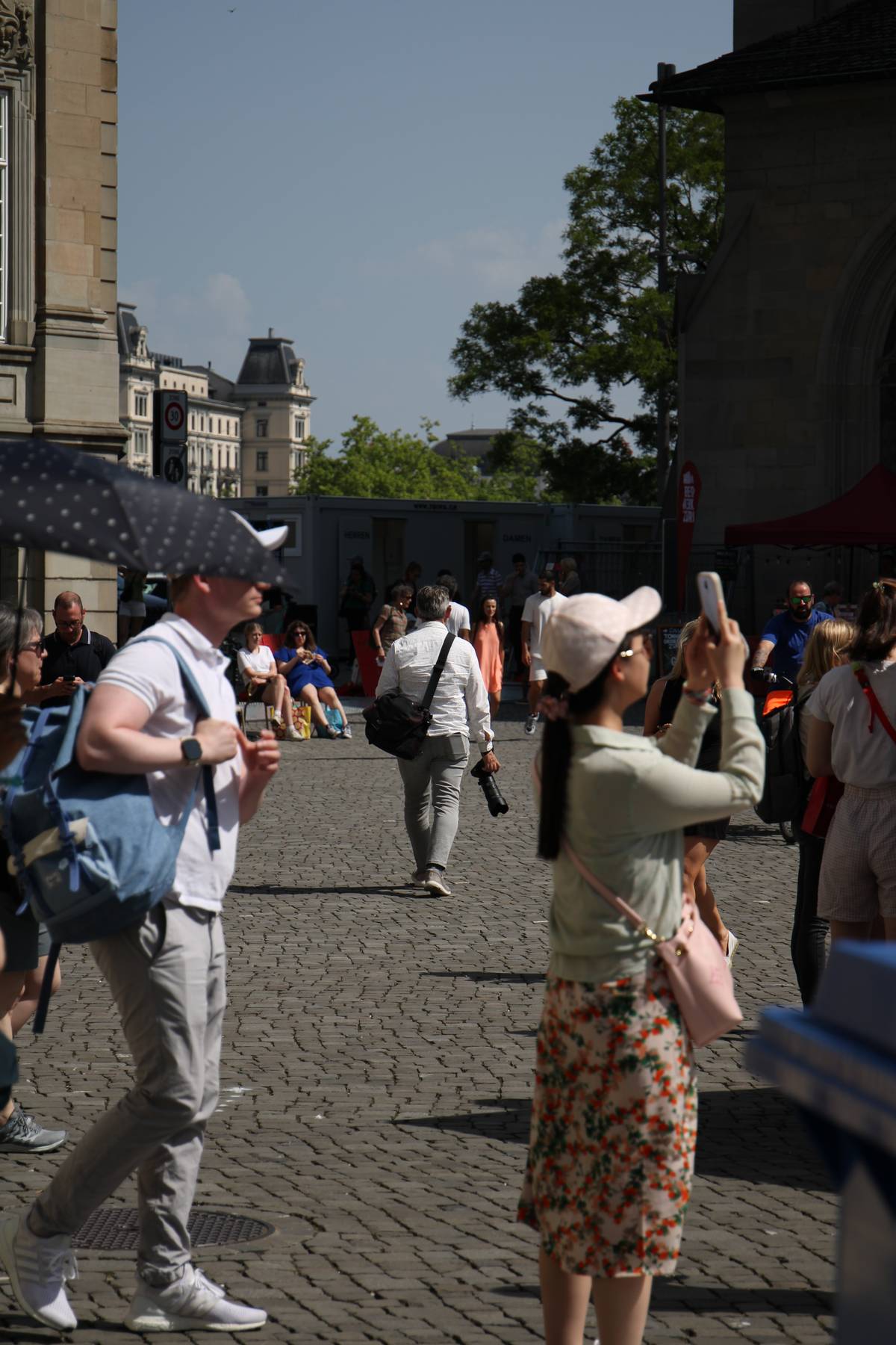 A photographer walks away dangling a camera with a long lens in his right hand
